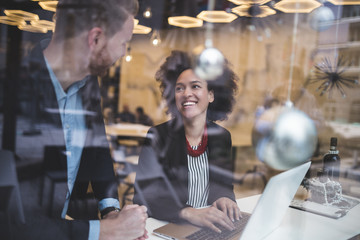 Multi racial business man and woman working together in modern cafe or restaurant. View from street through window glass.