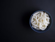 Cooked, thick udon noodles from Korea in small blue bowl, isolated on black background