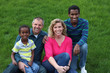 A multi-racial family, with caucasian parents sitting on the grass with their adopted, African sons.