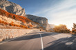 Asphalt road in autumn at sunrise. Landscape with beautiful empty mountain road with a perfect asphalt, high rocks, trees and sunny sky. Vintage toning. Travel background. Highway at mountains. Speed