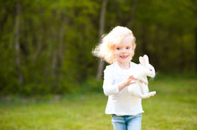 Laughing Baby Girl 3-4 Year Old Holding Small Rabbit Running In Meadow. Looking At Camera. Childhood.