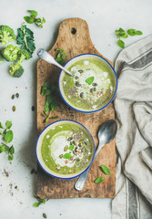 Wall Mural - Spring detox broccoli green cream soup with mint and coconut cream in blue bowls on rustic wooden board over marble background, top view. Clean eating, dieting, vegan, vegetarian, healthy food concept