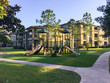 A typical apartment complex building with a central playground swing, stairs in suburban area at Humble, Texas, US. View from grassy backyard, surrounded by green trees in early morning with blue sky.