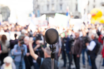 Wall Mural - Protest. Political rally. Demonstration. Microphone in focus, blurred crowd in background.