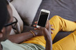 © wayhome.studio  - Unrecognizable stylish Afro American man wearing yellow jeans relaxing at home, lying on comfortable sofa, reading message on smart phone with black blank copy space screen for your information