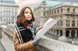 © EdNurg - A stylish woman in a coat with a scarf is guided by a map in the center of a European city, the concept of travel