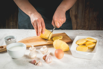 Person is cooking of a traditional French dish - potato gratin: potatoes, milk, cream, eggs, cheese, mushrooms, spices. Casserole. Vegetarian food. Female hands. 