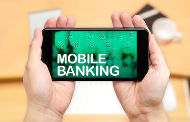 Poster - Watching two hand holding mobile phone with Mobile banking word on screen and blur desk office background,Digital marketing concept