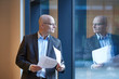 © Connect Images - Mature businessman holding paperwork looking through office window