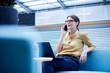© Connect Images - Businesswoman making smartphone call from sofa in office