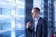© Connect Images - Businessman holding eyeglasses and looking through office window