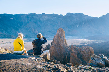 A couple of tourists sit on top of a mountain and admire volcanic landscapes at sunset in the Canary Islands, Spain