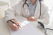 Medical doctor on white background with the stethoscope, looking at medical form and taking notes. Focus on the stethoscope and notes.