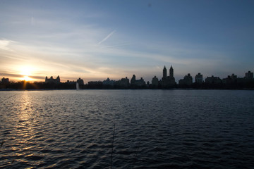 Wall Mural - Sunset reflects on lake and silhouette buildings with blue sky