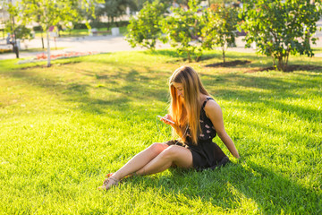 Girl listening to music streaming with headphones in summer on a meadow.