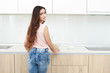 © Saksoni - Serious attitude. Young smiling lady standing in a kitchen.