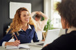 © nenadaksic - Young woman is talking to her client in the office, colleague is behind her, stretching hands