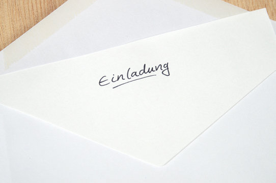 Einladung (Invitation), handwritten letter in white envelope, wooden background