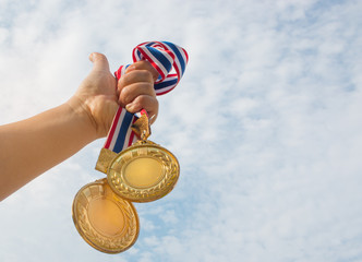 winner hand raised and holding two gold medals against blue sky. success award concept