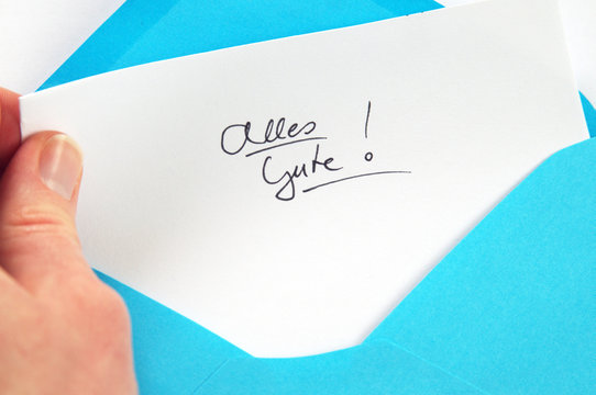 Alles Gute (All the best), hand holding handwritten letter in blue envelope
