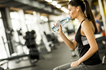 Attractive sport young woman drinking water while sitting and resting after workout