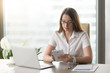 © fizkes - Serious businesswoman sitting at desk in front of laptop, using computer tablet. Female office worker checks email incoming text message on phablet. Handy mobile digital gadgets for business concept