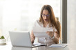© fizkes - Surprised young businesswoman reading letter at the desk in front of laptop. Woman feels shocked after receiving unexpected news in written message. Female entrepreneur holds notice about loan debt