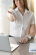 © fizkes - Smiling businesswoman offering handshake while sitting at desk in front of laptop in office. Female entrepreneur congratulates partners at the negotiating table. Hope for long-term business relations