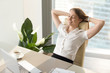 © fizkes - Joyed businesswoman keeping eyes closed while sitting at the desk with hands behind head. Happy lady leaning back in chair and relaxing with cup of coffee. Having positive feelings about work concept
