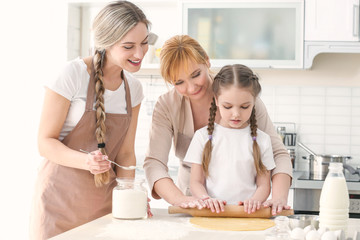 young woman with mother and daughter cooking in kitchen