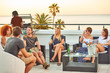 Attractive group of young people socialising on a rooftop with a view of the ocean while enjoying some alcoholic beverages and a gas barbecue on a warm summer sunset.