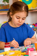 © Gennadiy Poznyakov - Small student girl painting in art school class. Child drawing by paints on table. Girl concentrates drawing. Craft drawing education develops creative abilities of children.
