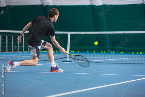 Plakat Młody człowiek w zamkniętym korcie tenisowym z piłką