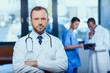 © LIGHTFIELD STUDIOS - portrait of confident doctor with stethoscope with colleagues behind in clinic