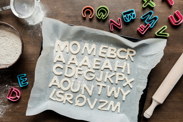 Wall Mural - top view of dough for cookies in forms of letters with rolling pin and baking paper, cookie dough