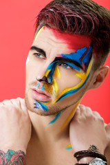 Wall Mural - portrait of young man with colored face paint on red background. Professional Makeup Fashion. fantasy art makeup