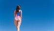 Beautiful young patriot USA back to camera on blue sky background in a swimsuit