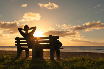 People enjoying nature. Woman relaxing on a park bench enjoying the sunset. 