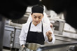 © Maskot - Young female chef tasting food from cooking pan at commercial kitchen