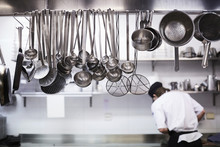 Utensils On Metal Rack With Chef Cooking In Background At Commercial Kitchen