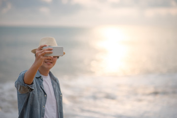 Wall Mural - Young Asian happy man taking a selfie shot with beautiful sunset on the beach by smartphone, vacation time and summer holiday travel concepts