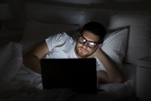 young man with laptop in bed at home bedroom