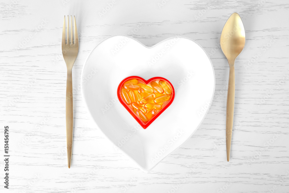 Heart-shape plate with fish oil capsules on wooden background