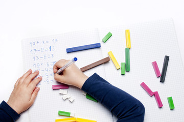 Open exercise book with colored plastic math learning tools number rods on white background. Close-up of children's hands. solving mathematics examples. Educational and school concept.