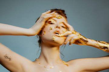 Motion blur beauty portrait of young fashion model with golden make-up and metallic gold nails on blue background. 