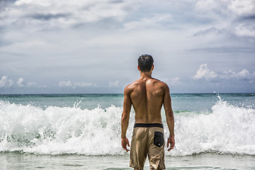 Handsome young man standing on a beach in Phuket Island, Thailand, shirtless wearing boxer shorts, showing muscular fit body