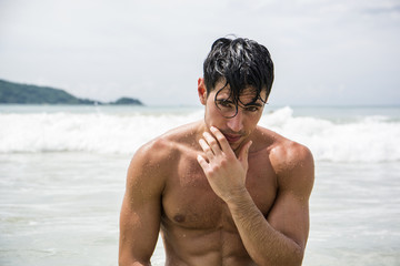 Handsome young man standing on a beach in Phuket Island, Thailand, shirtless wearing boxer shorts, showing muscular fit body