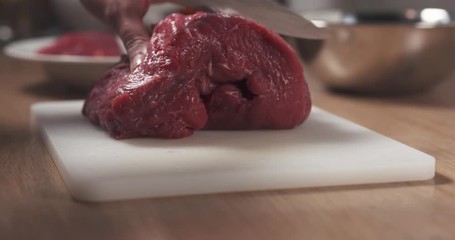 Wall Mural - Slide shot of young female hand cutting raw beef with a knife on plastic board, 4k prores footage