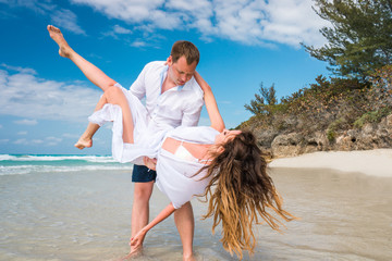 Canvas Print - Handsome man holds on his hands beautiful woman with long curly hair in white swimsuit and beach dress on the coastline