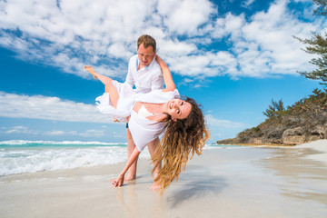 Sticker - Handsome man holds on his hands beautiful woman with long curly hair in white swimsuit and beach dress on the rocks coastline